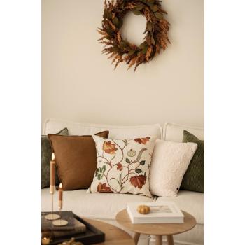 Putetrekk i brun, grønn og hvit med brodert pute i front i sofa